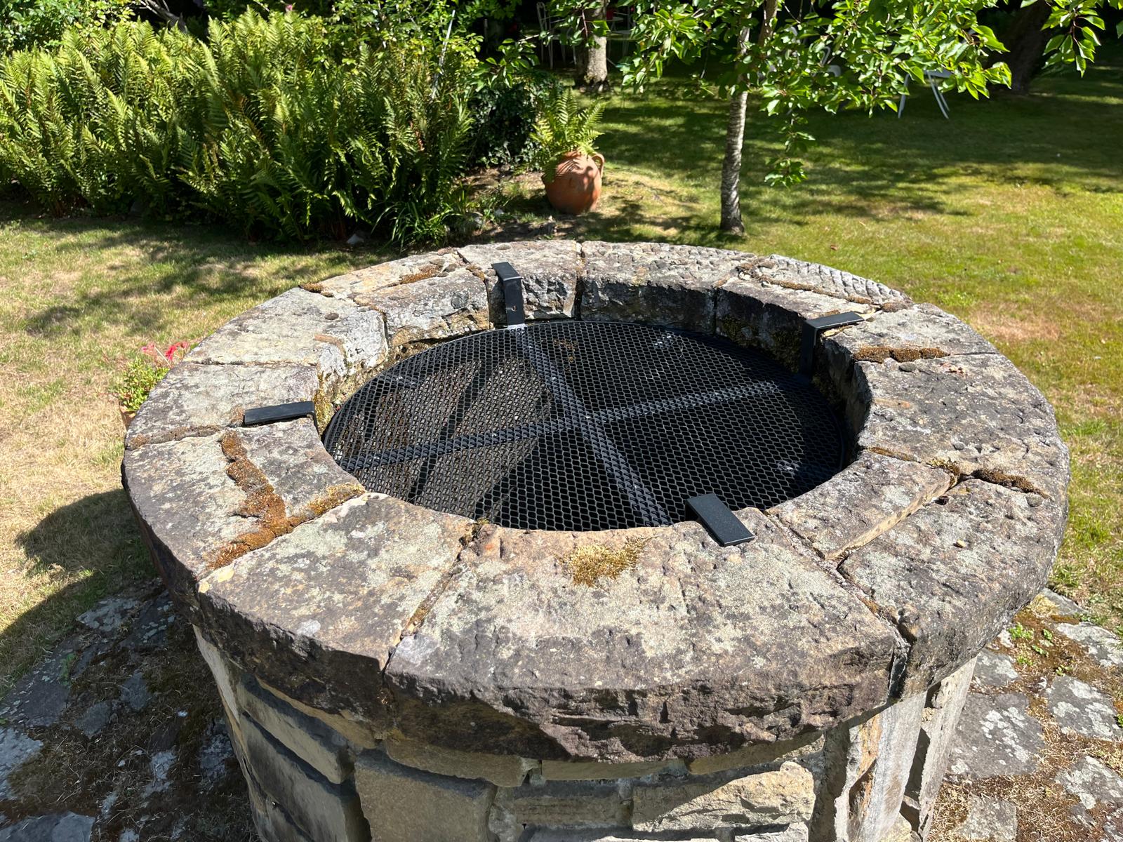 Grille circulaire en acier sur un puits en pierre dans un jardin