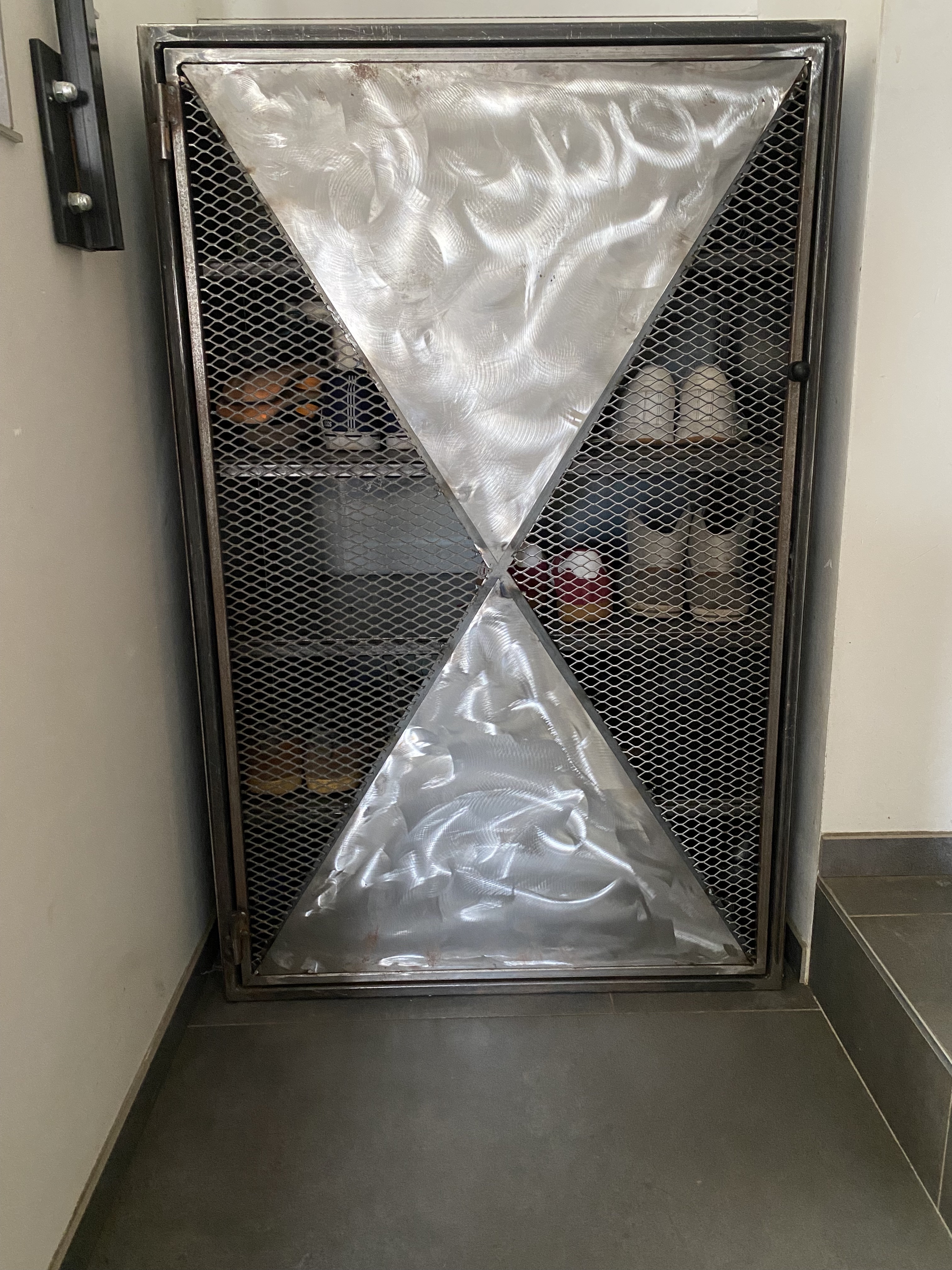 Meuble à chaussures en acier sous un escalier, avec porte à motifs géométriques